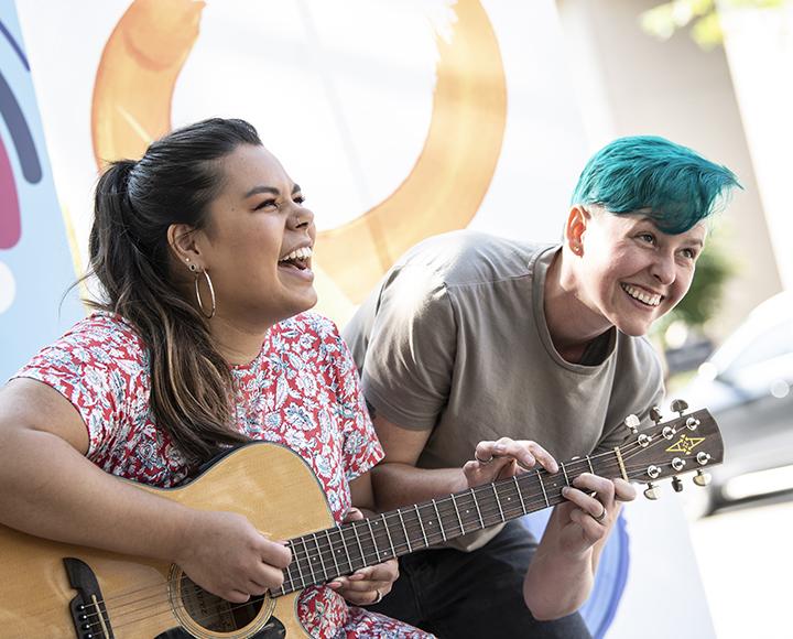 Two students playing a duet on a guitar during Parking Day